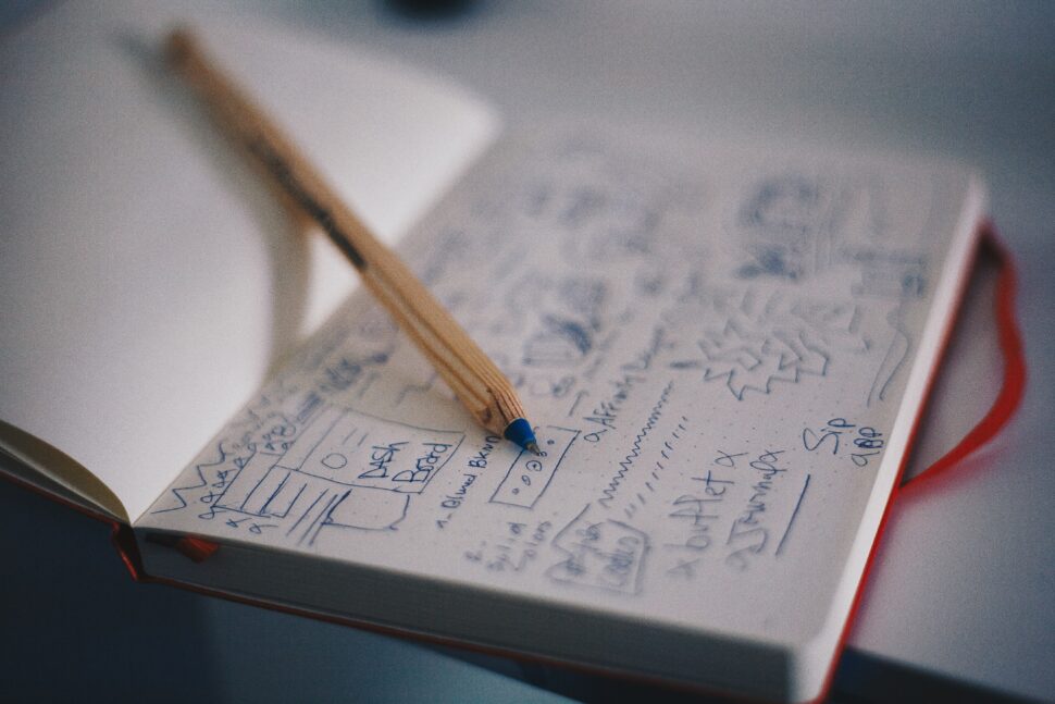 blue ballpoint pen on white notebook drawing a web design system